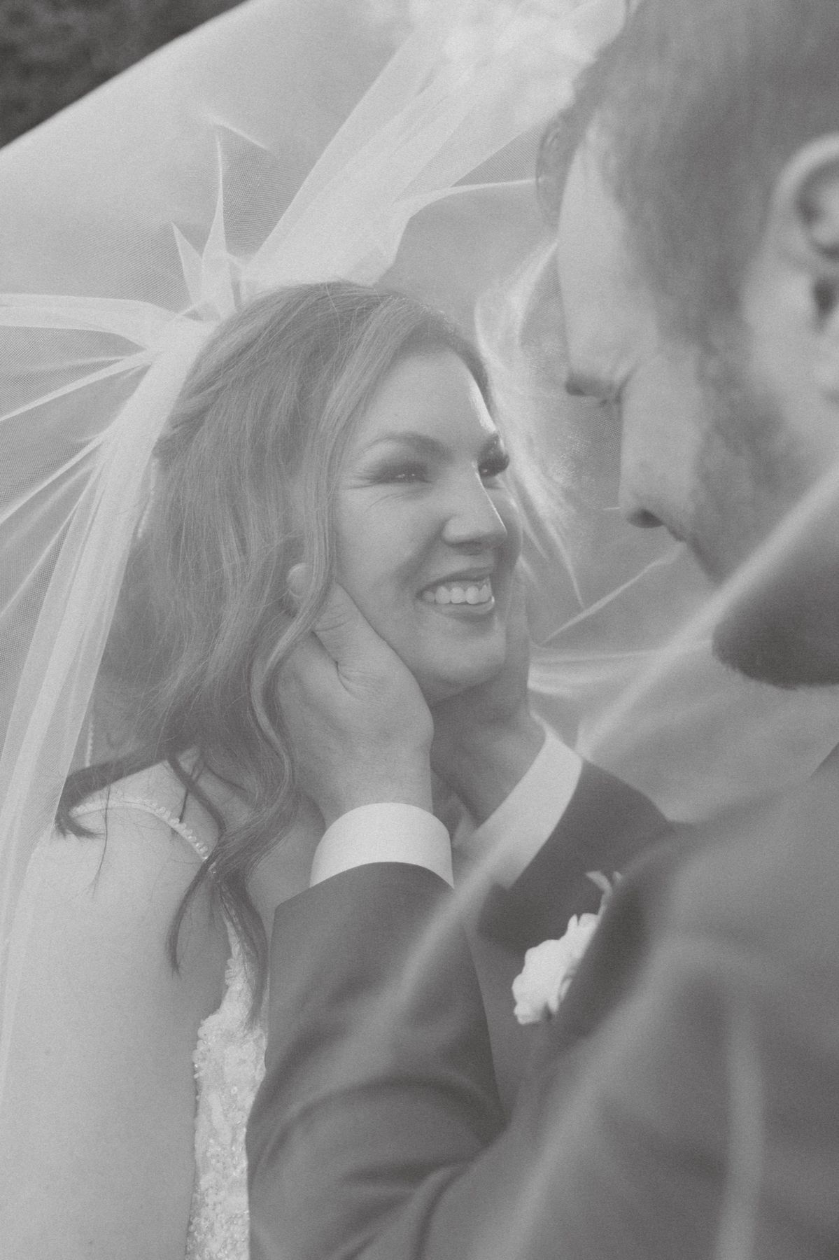 Bride and groom laughing beneath her veil, black and white